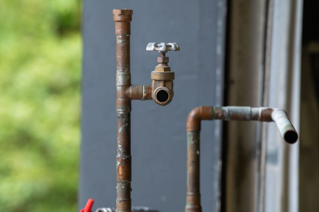 pexels-photo-35016079 Detailed view of an old, rusty industrial water pipe with valve, conveying vintage industrial aesthetics.